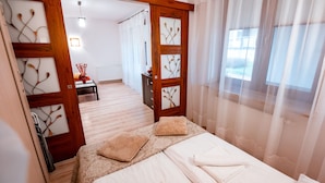 A hotel room with a bed, a wooden wardrobe, a small table with a vase, and a view through sheer curtains. - Apartamenty Sun & Snow Kraszewskiego (Krynica-Zdroj)