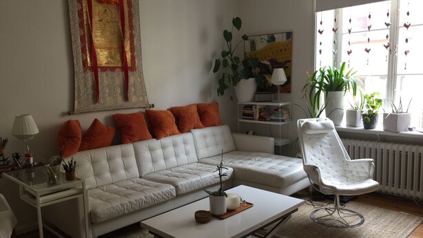Una sala de estar moderna con un sofá blanco, cojines naranjas, un sillón blanco, una mesa de centro de vidrio y una estantería.