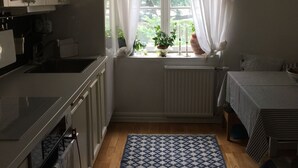 Cocina compacta con armarios blancos, horno empotrado y ventana con cortinas translúcidas.
