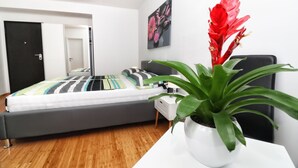 Un dormitorio moderno con cama, una mesita de noche con planta en maceta, una mesilla auxiliar y un cuadro colgado en la pared.