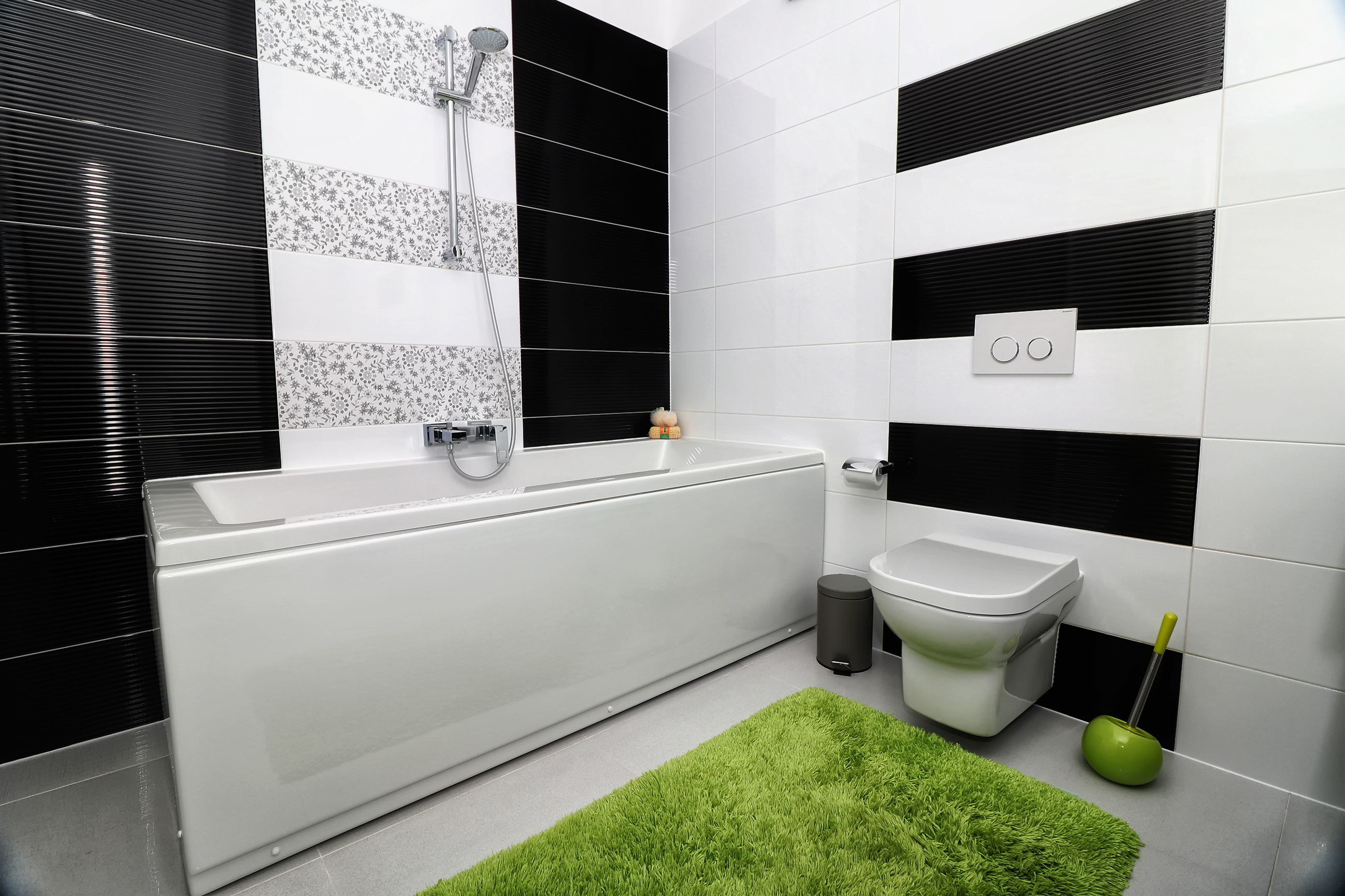 Ein modernes Badezimmer mit einer weißen Badewanne, einer Toilette und einer Fußmatte in Grün.