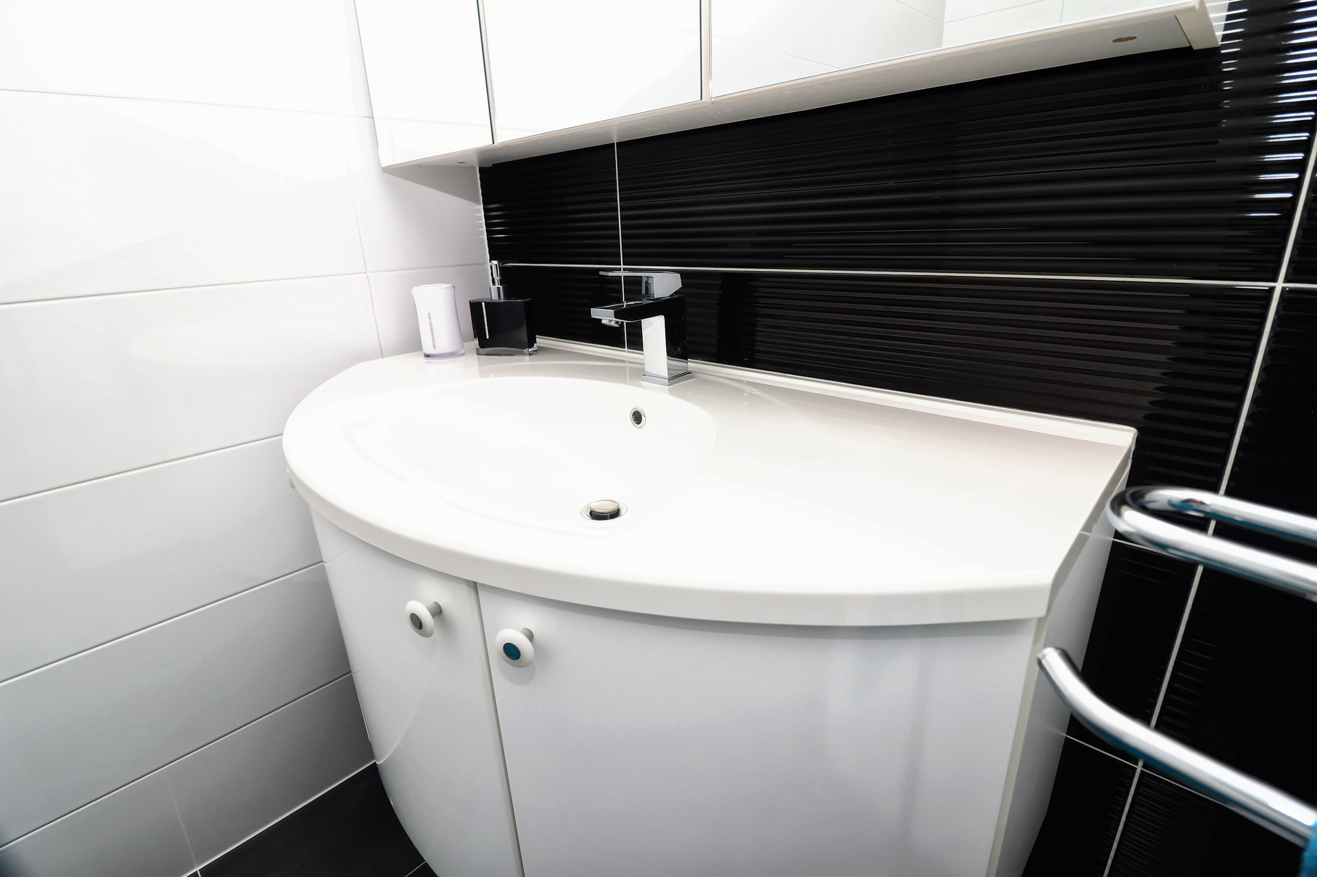 Um banheiro moderno com pia branca, backsplash de azulejo preto e vaso sanitário branco.