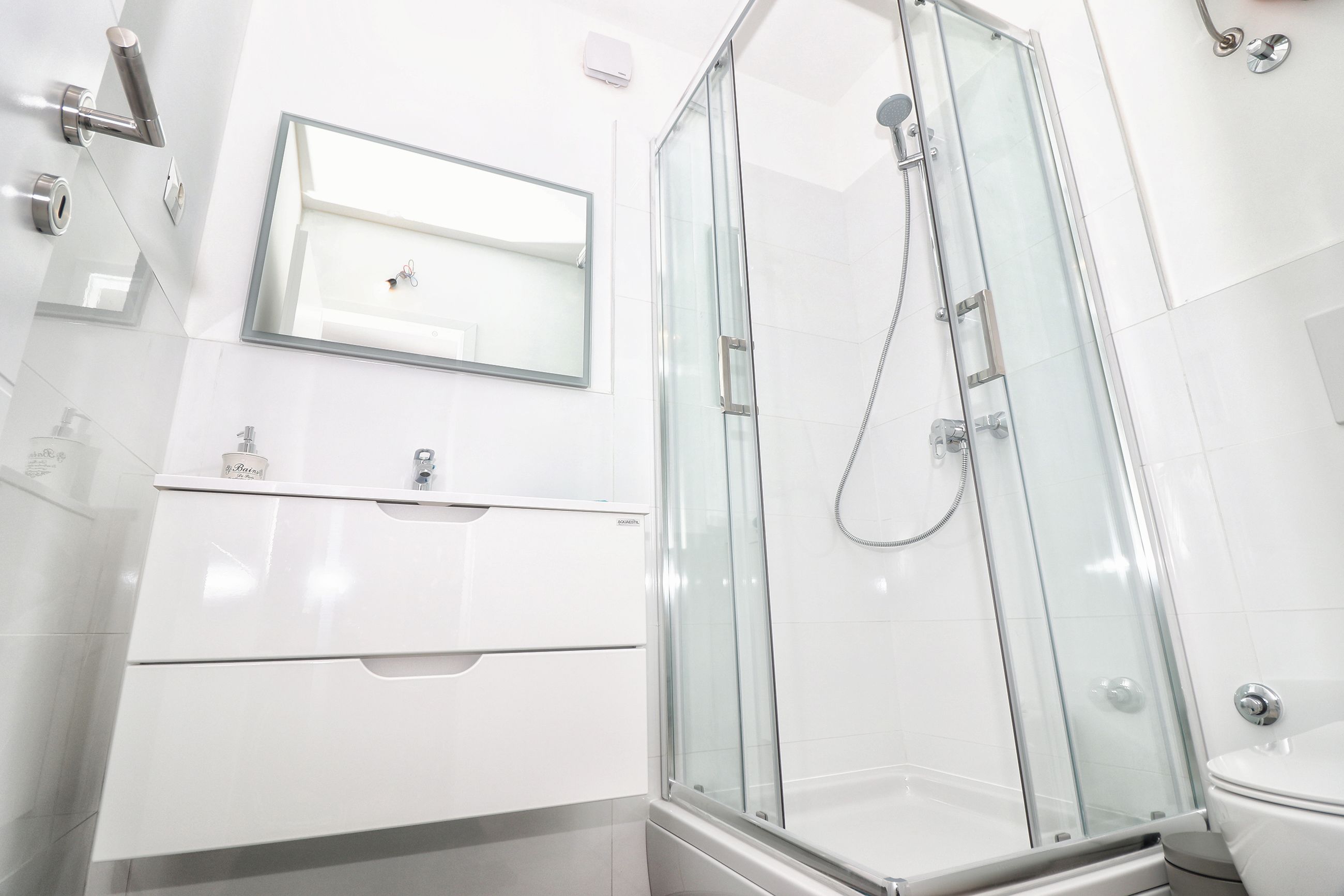 Un baño moderno con ducha de vidrio, lavamanos blanco y espejo sobre el lavamanos.