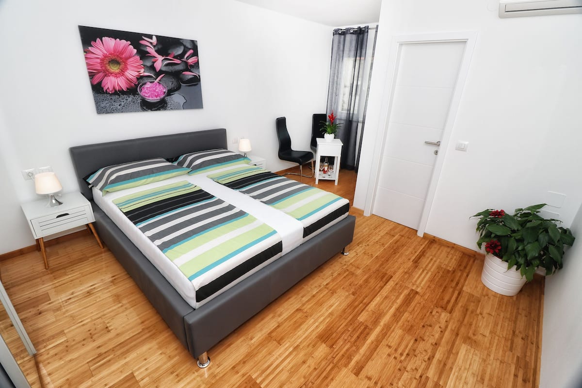 A modern bedroom with a bed, bedside tables, a chair, a potted plant, and a door.