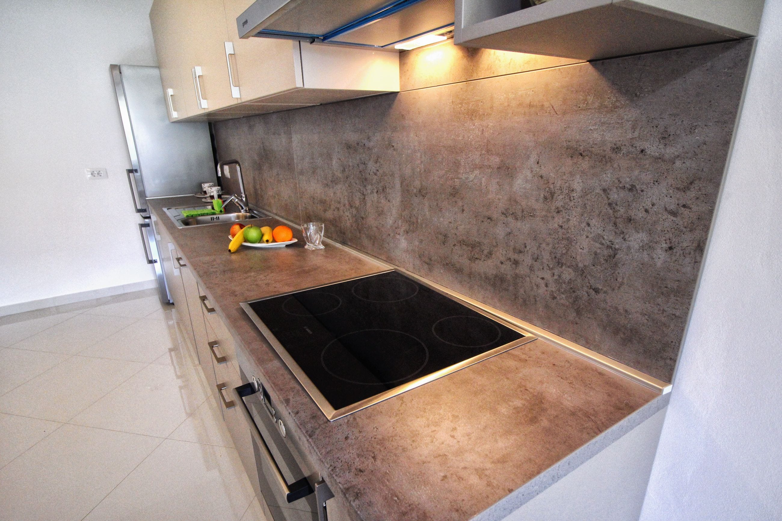 A modern kitchen with a built-in stove, a sink, and a countertop with fruits and a glass.