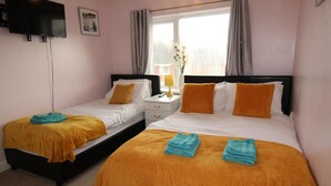 A hotel room with two beds, each with a white and orange bedspread, and a small bedside table with a lamp. - Dryden House (Chesterfield)