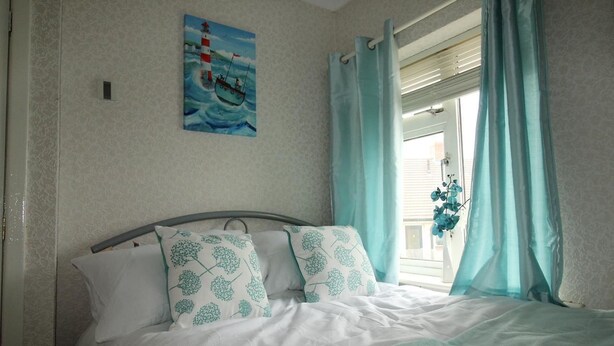 A bedroom with a bed, a painting of a lighthouse, and a window with curtains. - Dryden House (Chesterfield)
