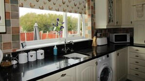 A kitchen with a washing machine, a microwave, and a window with a view of the outside. - Dryden House (Chesterfield)