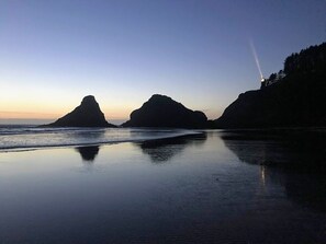 Una playa con aguas tranquilas que reflejan las siluetas de formaciones rocosas.