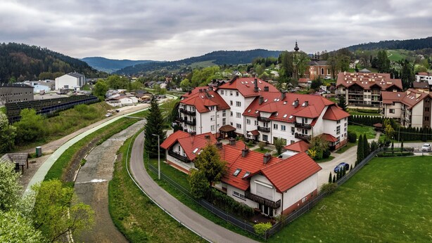 A residential area with multiple two-story houses, a church, and a bridge in the background. - Apartamenty Sun & Snow Nad Potokiem (Krynica-Zdroj)