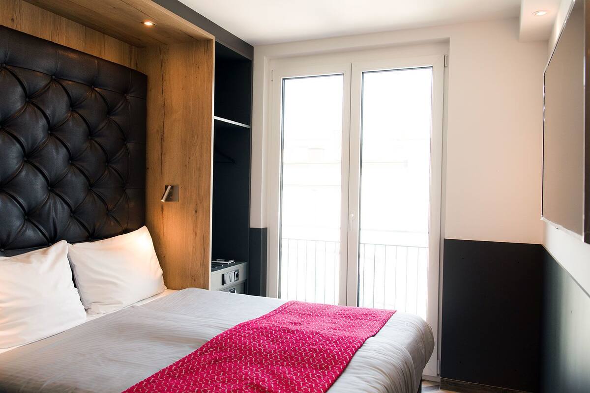 A modern bedroom with a tufted headboard, a bed with white linens and a pink blanket, a built-in wardrobe, and a sliding glass door to the balcony.