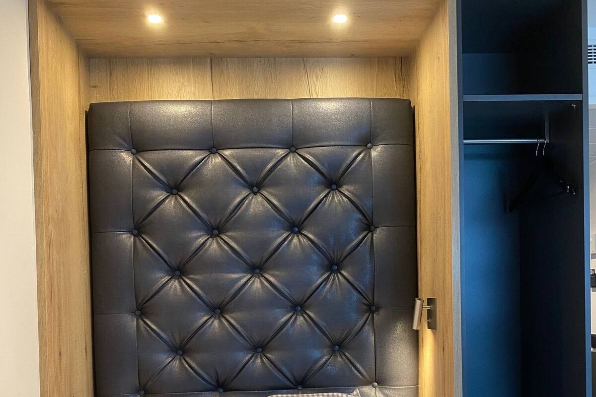 A bed with a tufted headboard, a checkered pillow, and a bedside table with a lamp.