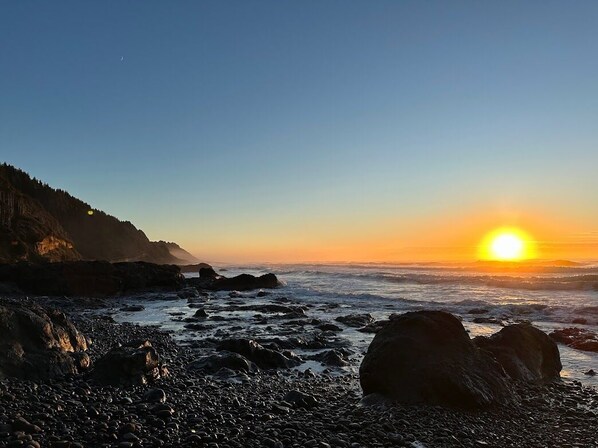 Experience the serene coastal atmosphere, where ocean waves gently lap against the shore and a dramatic cliff rises in the background.