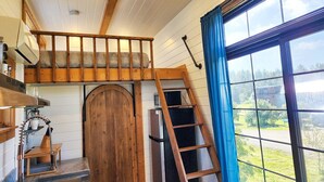 A rustic interior with a wooden staircase, a large window with a view, and a door with a unique arch design.