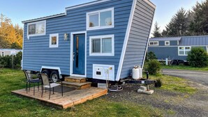 A blue mobile home with a front porch and a small attached trailer.