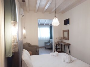 A hotel room with a bed, a desk, a chair, and a hanging light fixture.