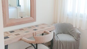 A room with a wooden floor, a grey armchair, a small round table with a mirror, and a window with sheer curtains. - Lefkada Princess (Lefkada)