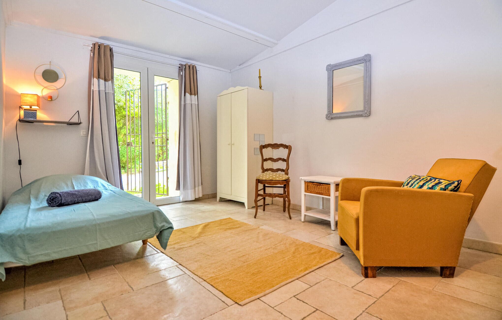 A room with a bed, a yellow armchair, a wooden chair, a small table, and a wardrobe.