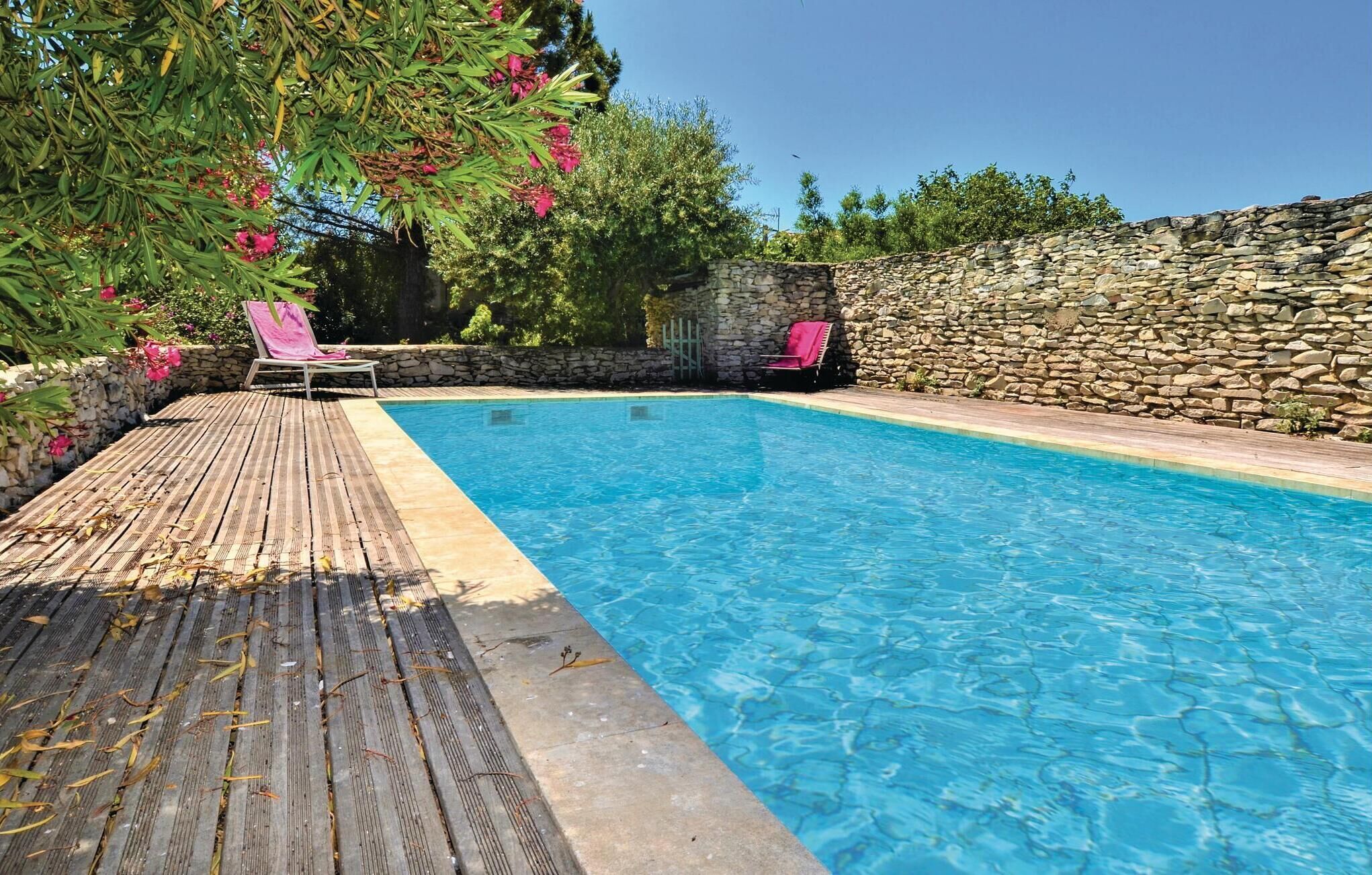 Una piscina azul cristalina con una terraza de madera y un muro de piedra.