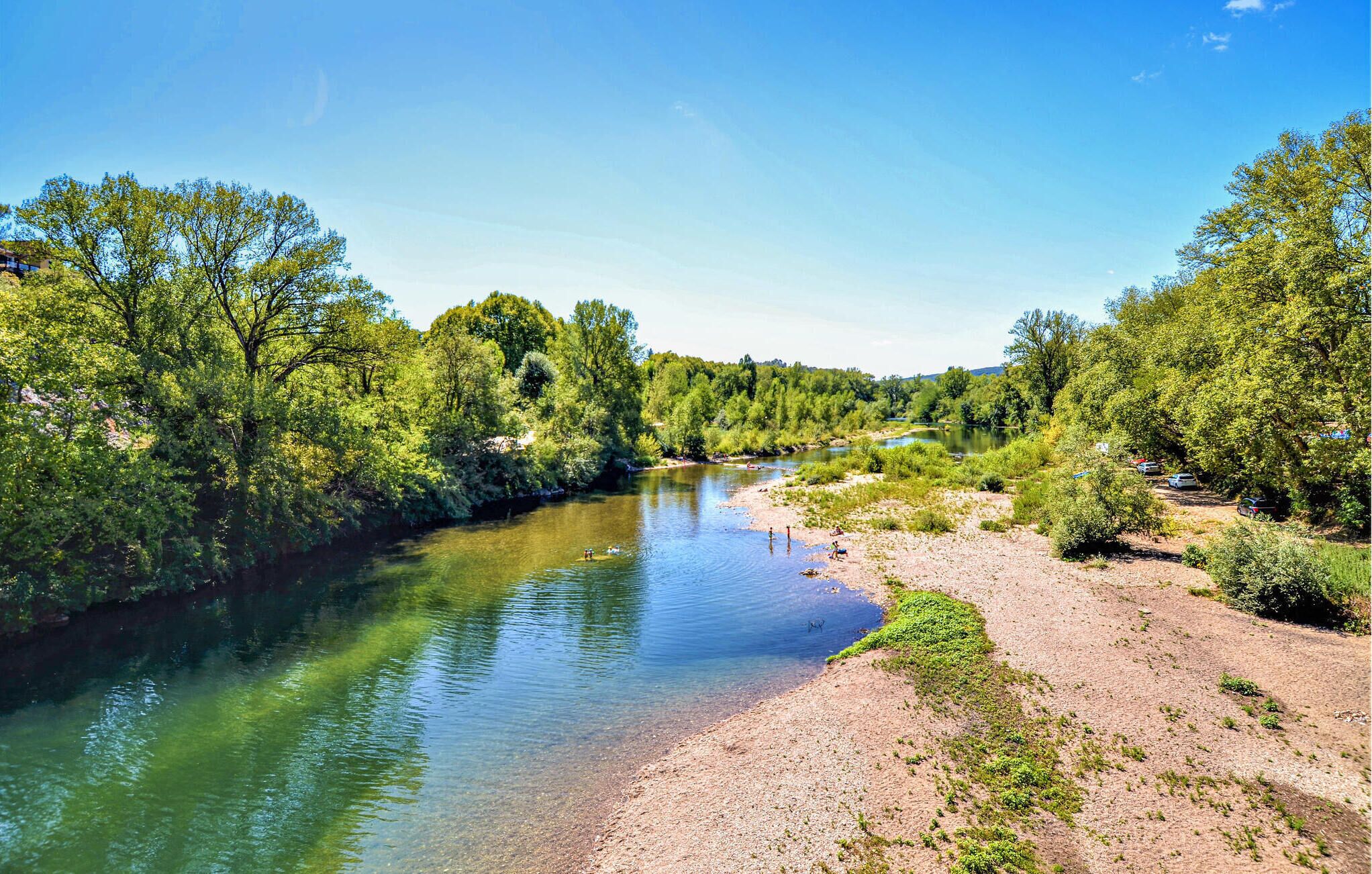 Un riu d'aigua cristal·lina, envoltat de boscos verds i una riba sorrenca.