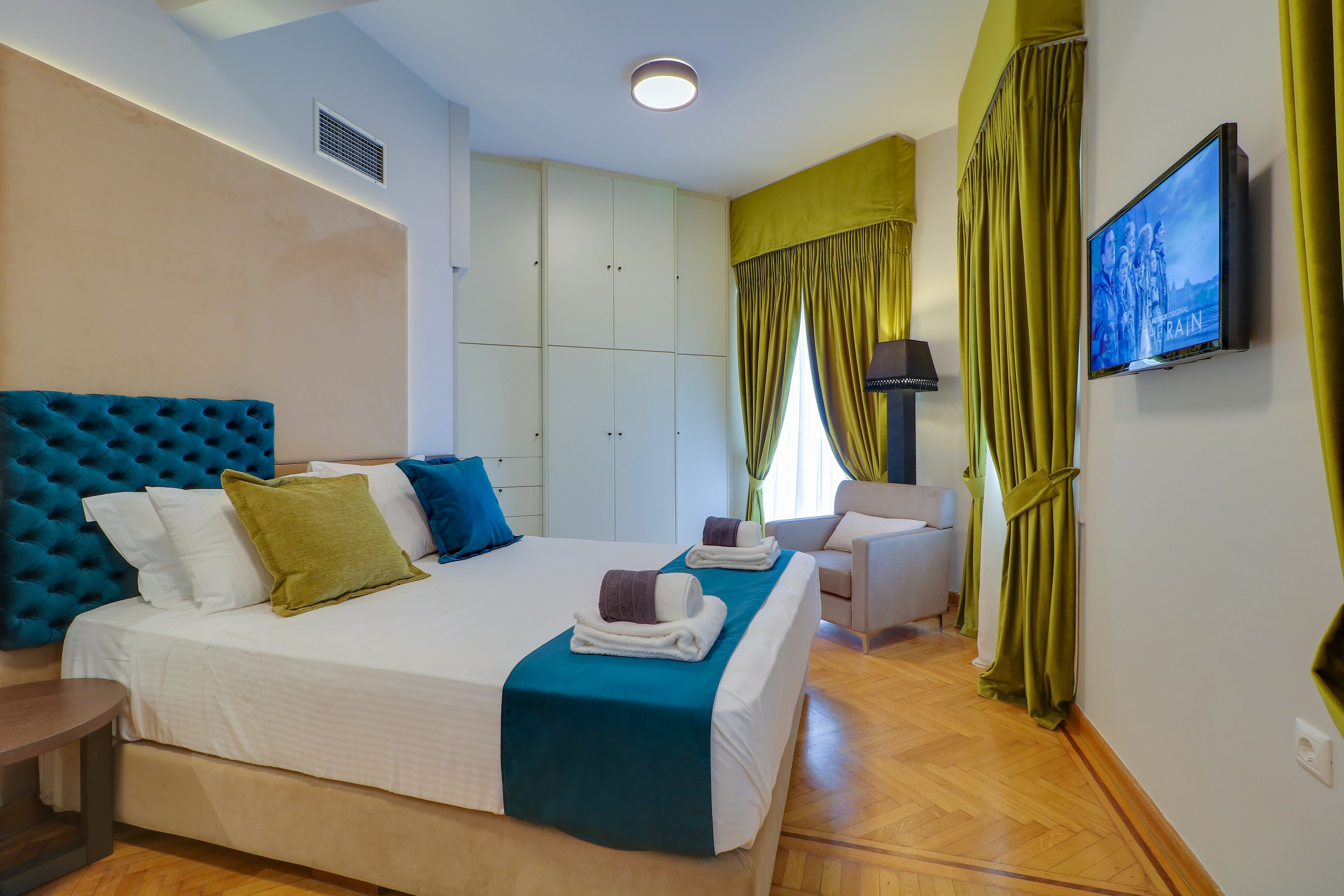 A hotel room with a large bed, a chair, a TV, and a wardrobe.