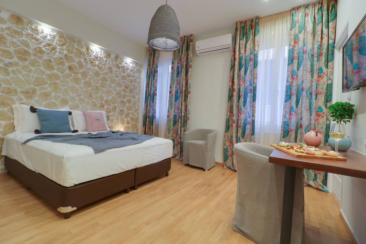 A bedroom with a stone wall, a bed with pillows, a chair, a table with food, and an air conditioning unit.
