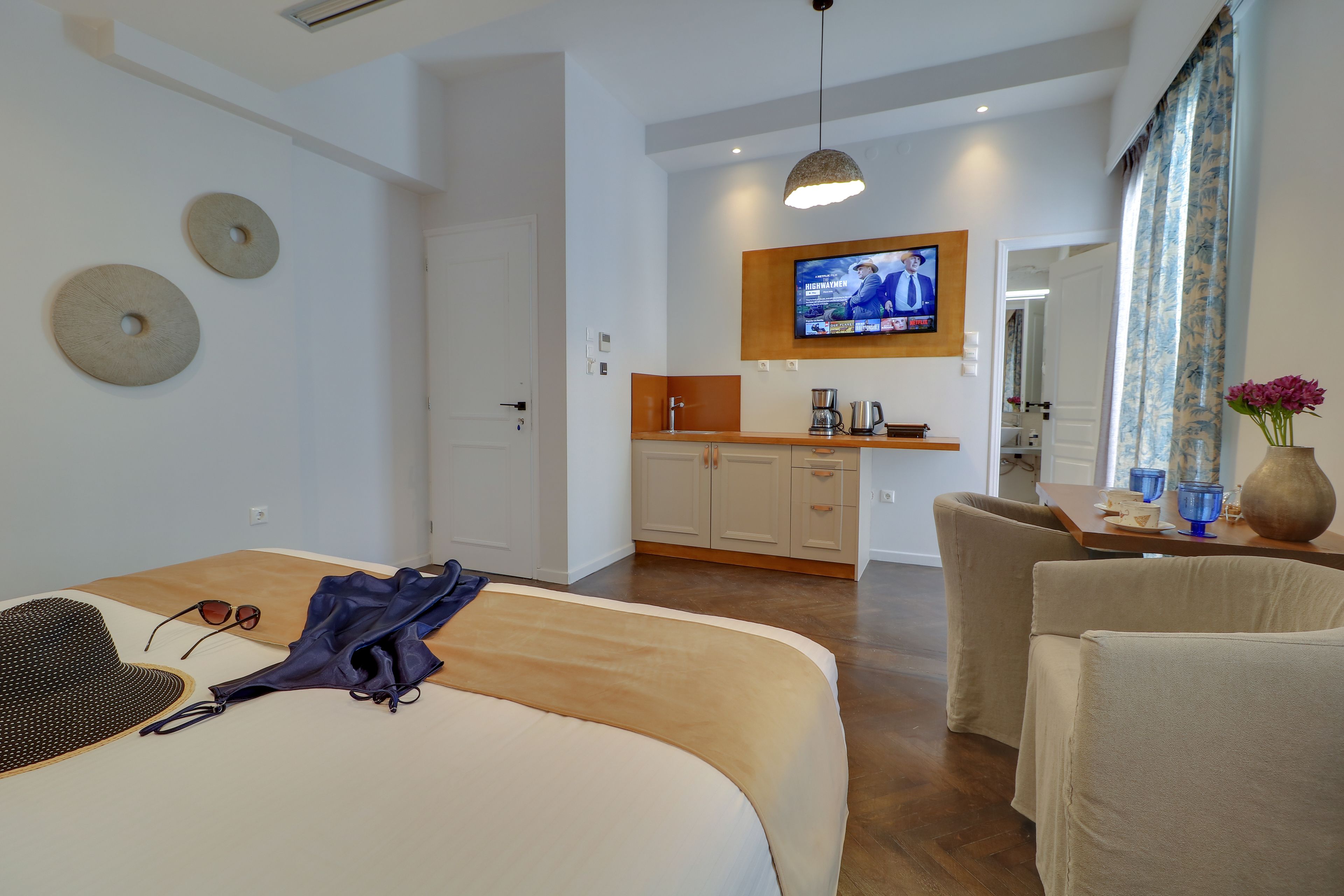 A hotel room with a bed, a desk, a chair, a television, and a kitchenette.