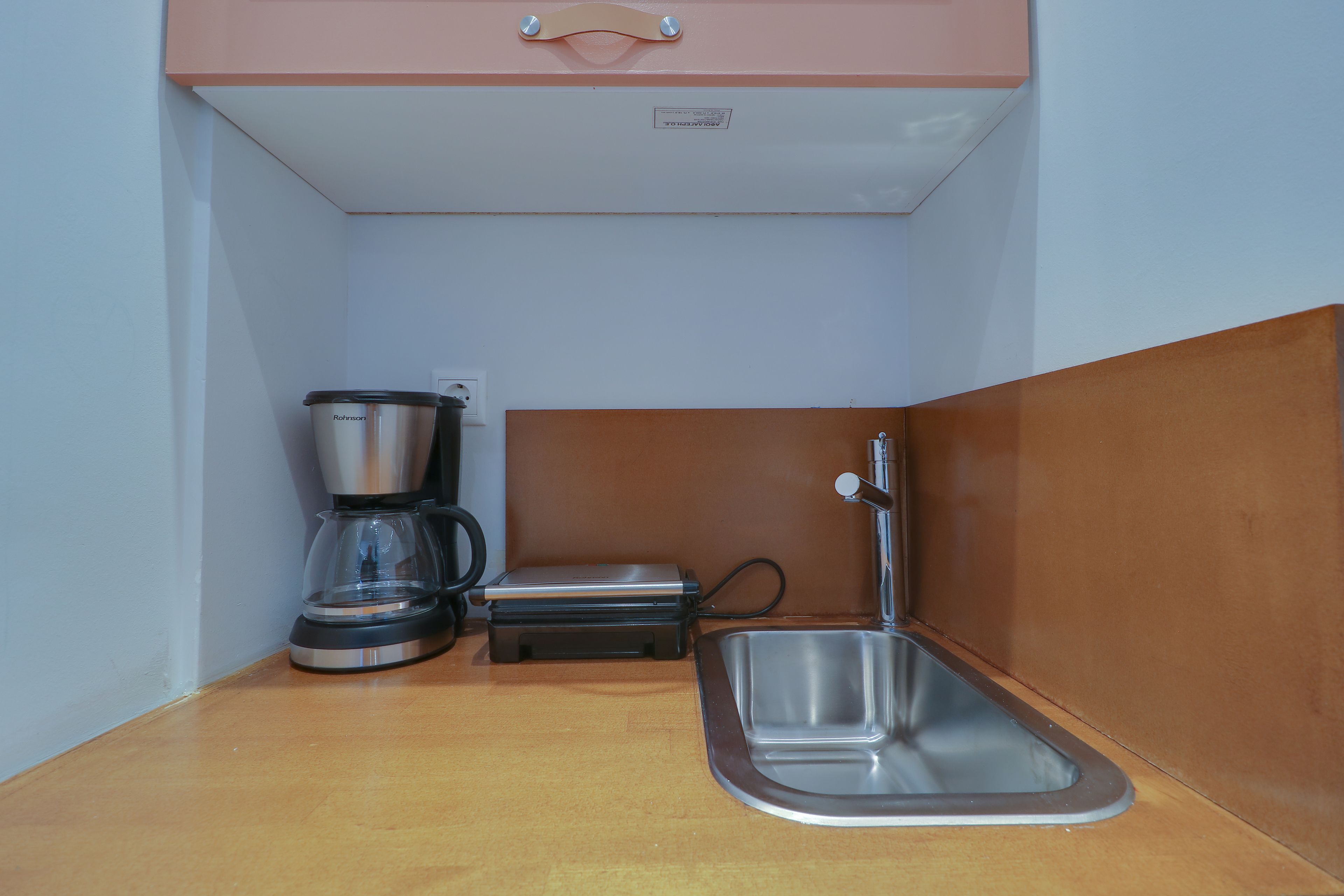 A compact kitchenette with a coffee maker, a small sink, and a cabinet.
