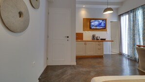 A modern living room with a wooden floor, a sofa, a TV mounted on the wall, and a kitchen area with wooden cabinets and a countertop. - AthiNN Residence (Athens)
