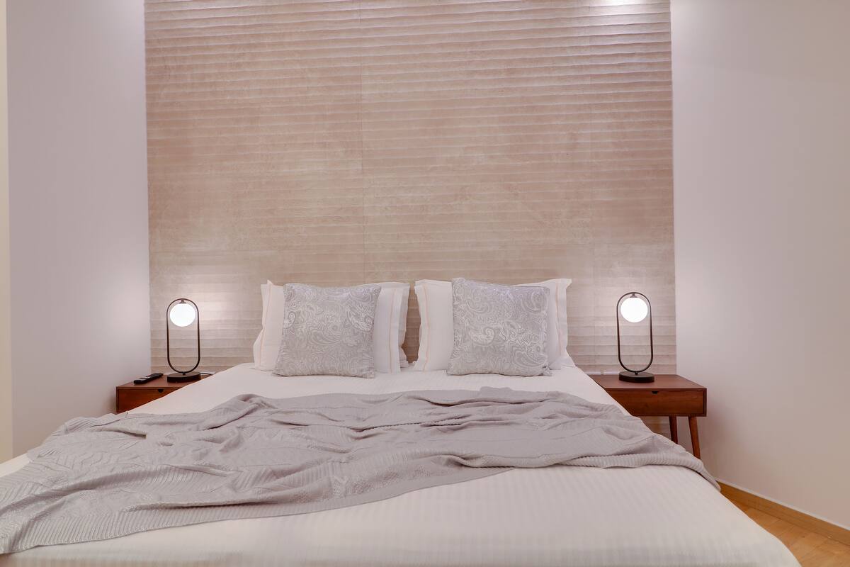 A neatly made bed with a grey blanket, two bedside lamps, and a wooden nightstand.