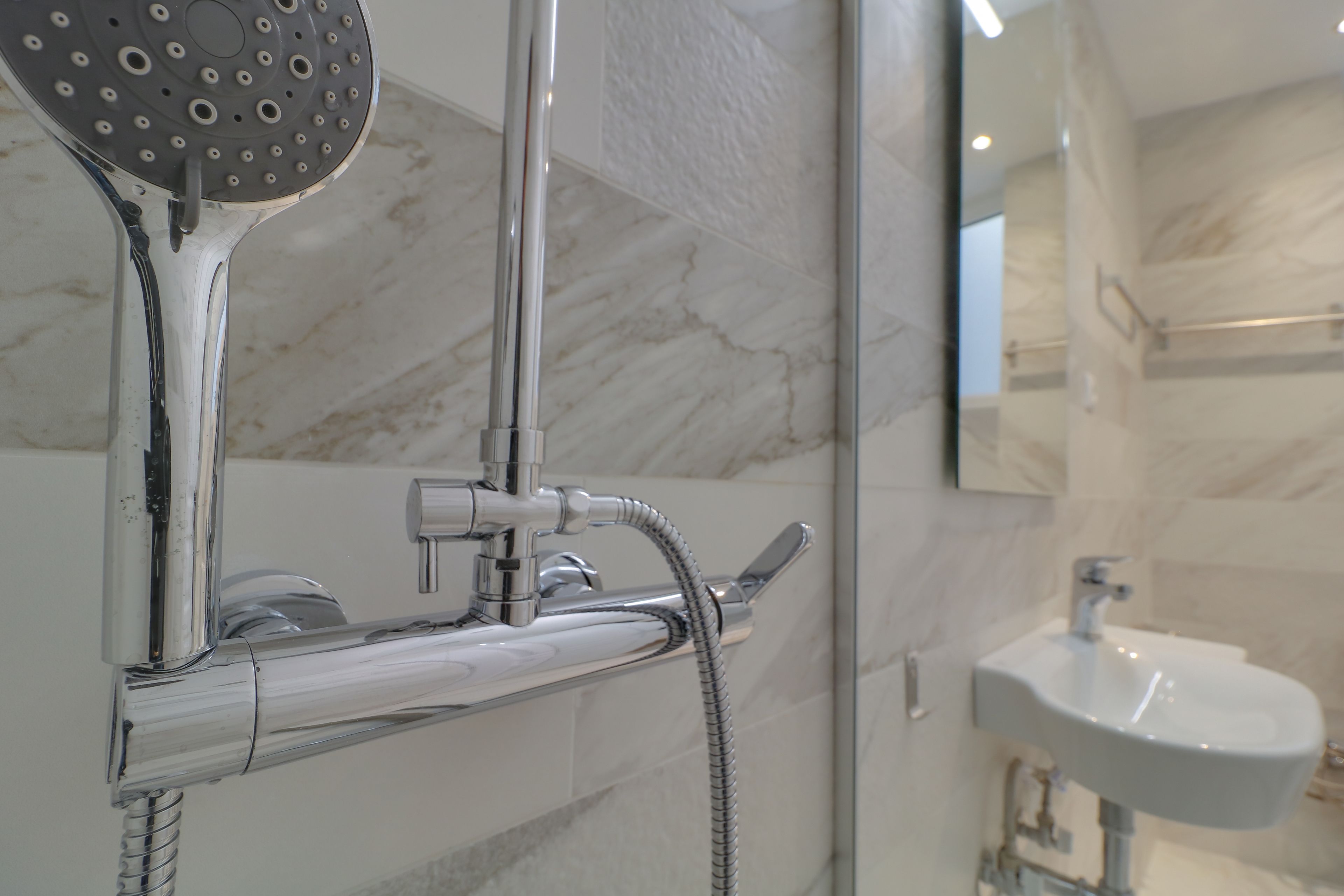 Une salle de bain moderne avec une douche, un lavabo et un mur en marbre.
