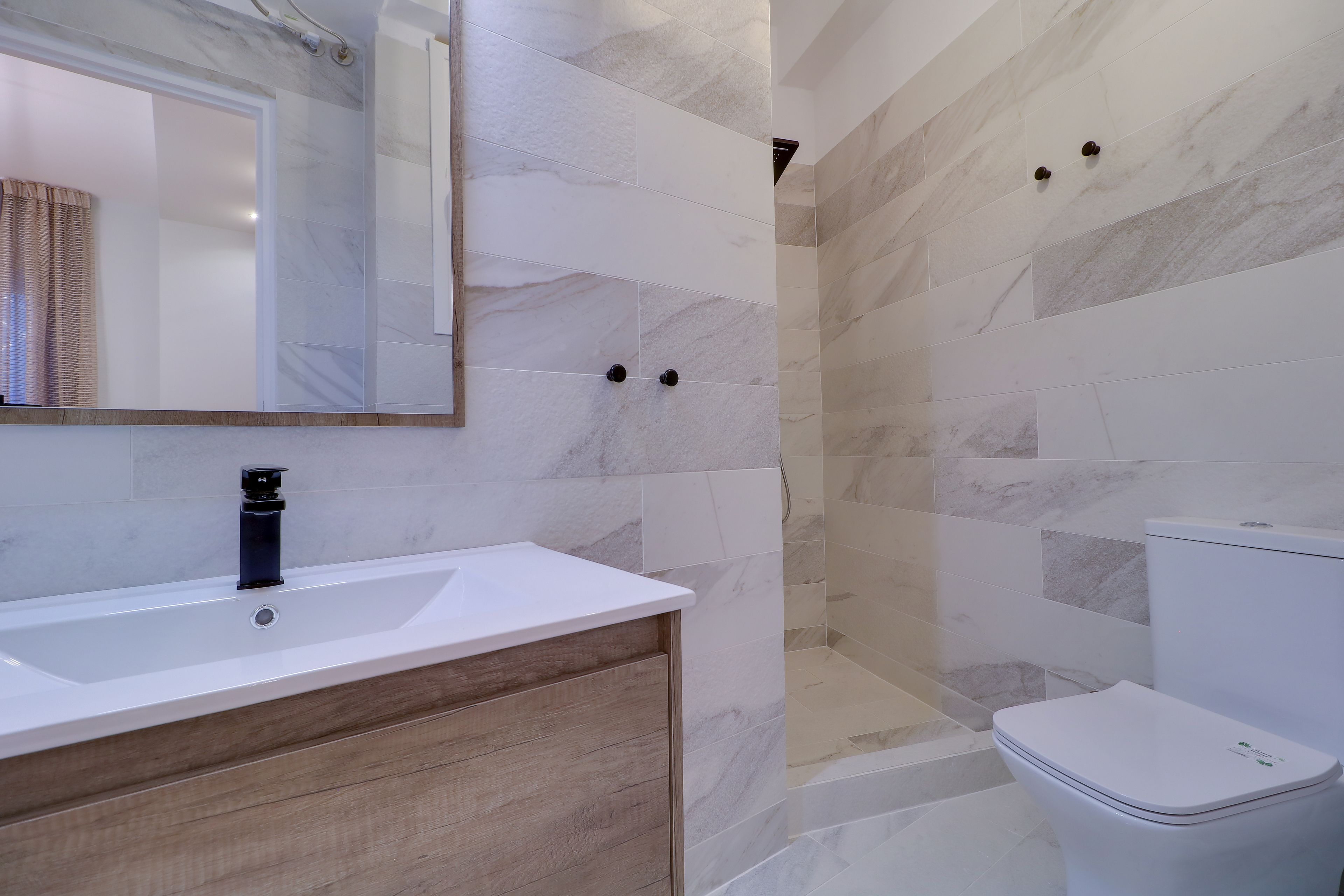 Un baño con lavamanos blanco, tocador de madera, espejo, cabina de ducha y retrete.