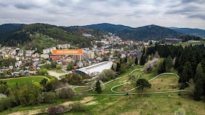 Une vue panoramique d’une ville avec un grand parc sportif, entourée de bâtiments résidentiels et de collines.