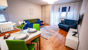 Un salon moderne comprenant un coin repas, un canapé bleu, un fauteuil vert et une petite table mise pour deux personnes.
