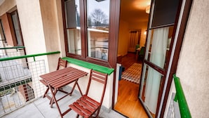 Un balcon avec une table et des chaises en bois, une rambarde verte et une vue sur l’intérieur.