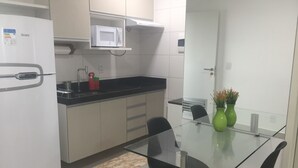 Eine moderne Küche mit einem weißen Kühlschrank, einer Mikrowelle und einem Spülbecken. Es gibt einen Glastisch mit zwei Stühlen und eine Vase mit Blumen.