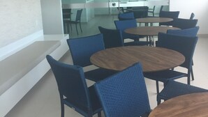 Ein moderner Konferenzraum mit runden Tischen und blauen Stühlen, weißen Wänden und einer Glaswand.