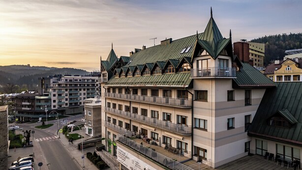 A multi-story hotel with a distinctive green roof and multiple balconies. - Apartamenty Sun & Snow Pułaskiego (Krynica-Zdroj)