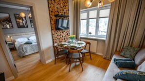 A modern living room with a dining area, wooden log wall, large windows, and a flat-screen TV. - Apartamenty Sun & Snow Pułaskiego (Krynica-Zdroj)