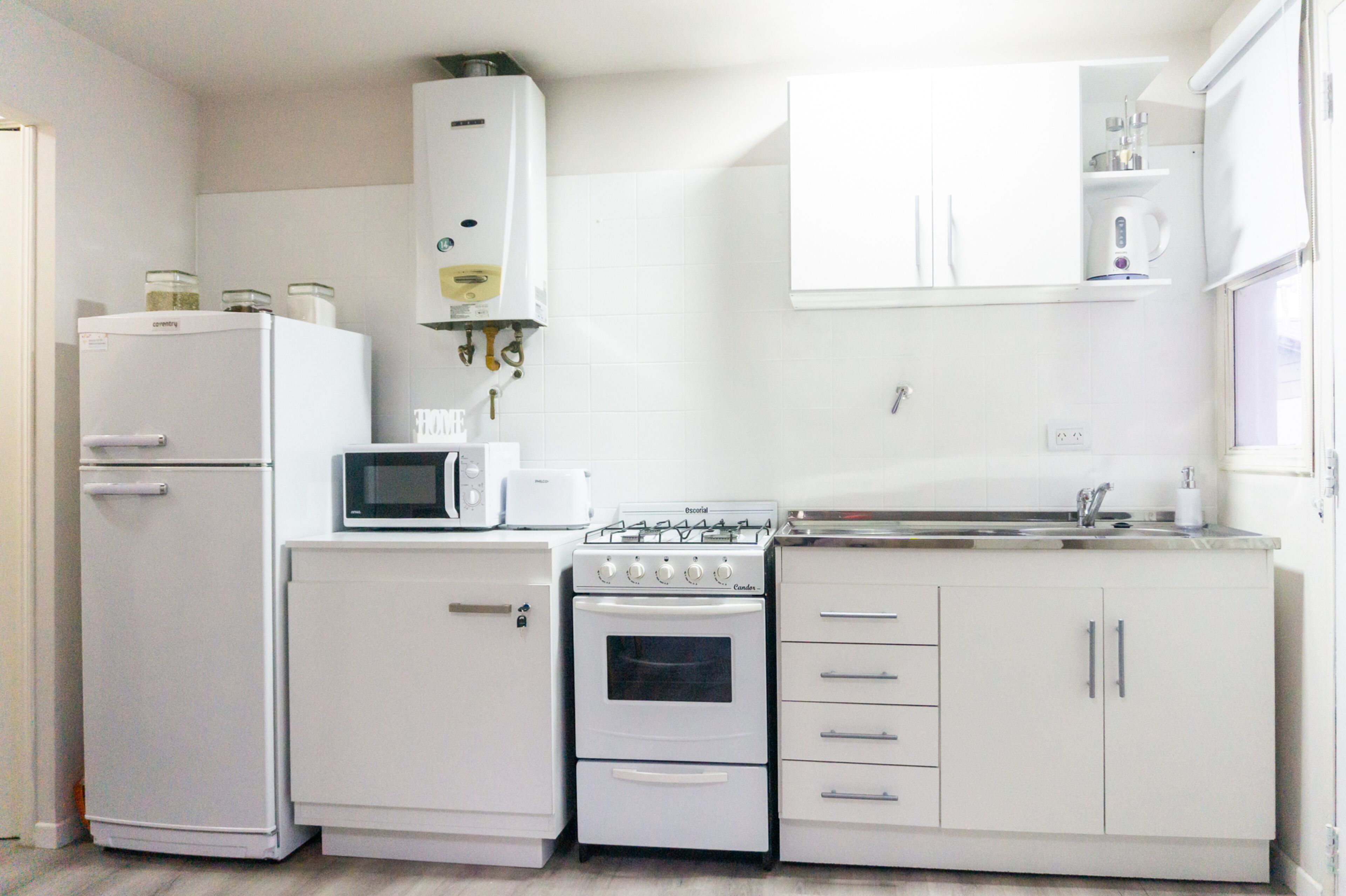 Uma cozinha compacta com geladeira, micro-ondas, fogão, forno e armários brancos.