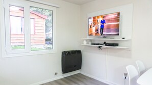 A room with a TV mounted on a white wall, a window with a view of a house, and a white chair. - Gente del Sur - Gobernador Paz (Ushuaia)