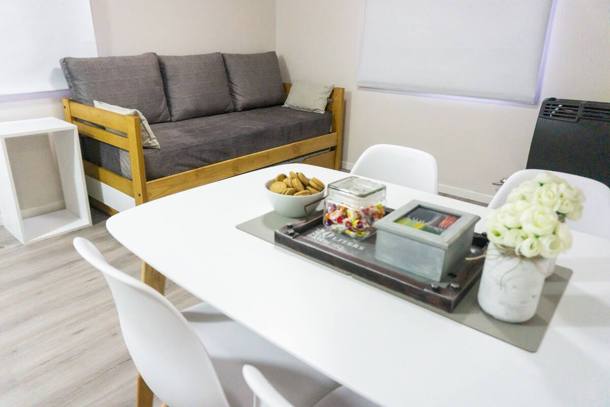Ein modernes Zimmer mit einem weißen Tisch, einem grauen Sofa, einer Schale Kekse, einem Glasbehälter und einer Vase mit weißen Blumen.