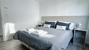 A modern bedroom with a large bed, grey bedding, and a bedside table with a lamp. - Gente del Sur - Gobernador Paz (Ushuaia)