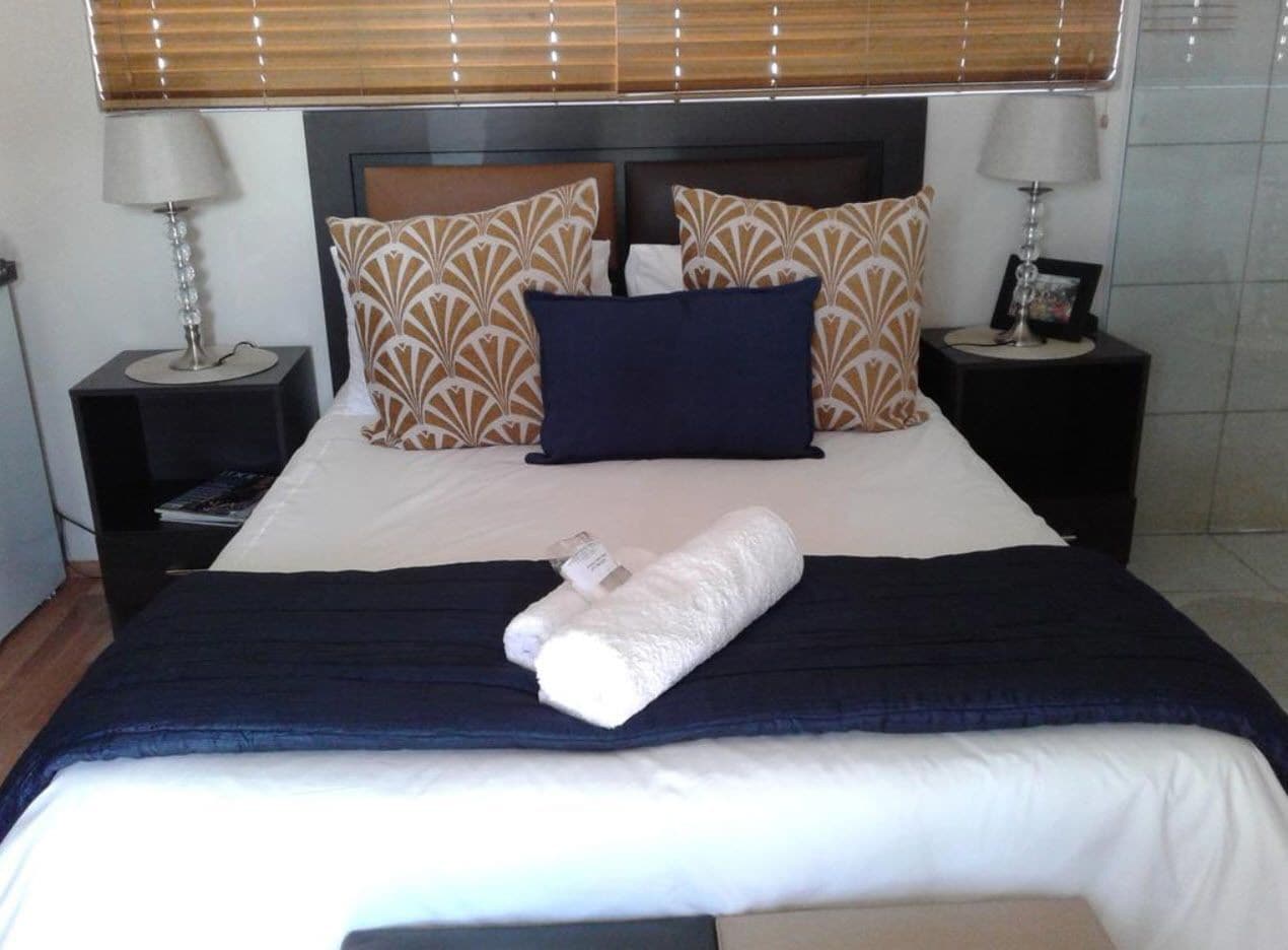 A neatly made bed with patterned pillows, a folded towel, and two bedside lamps on black nightstands.