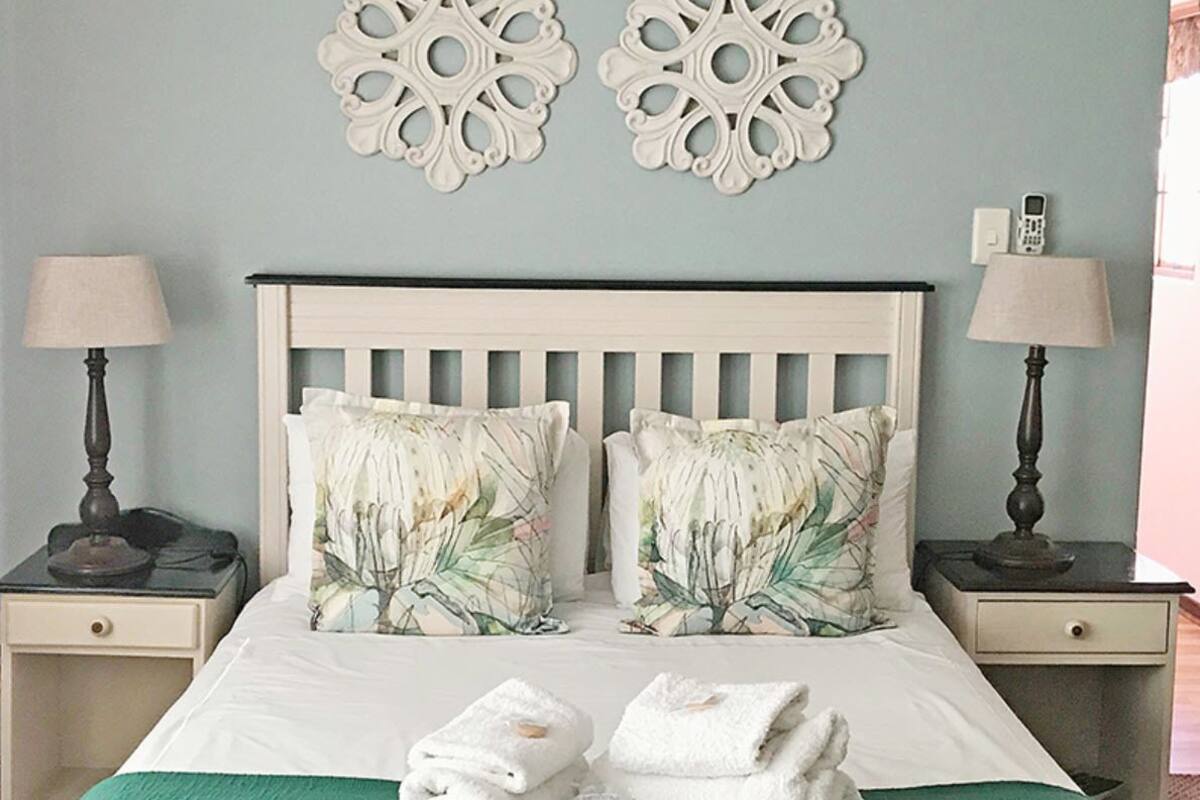 Een net opgemaakt bed met bloemenkussens, twee nachtkastjes met lampen en decoratieve wandkunst.