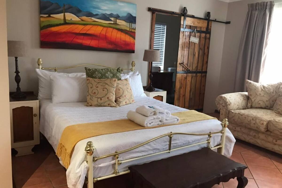 Een netjes ingerichte slaapkamer met een bed, nachtkastje, lamp en een schilderij aan de muur.