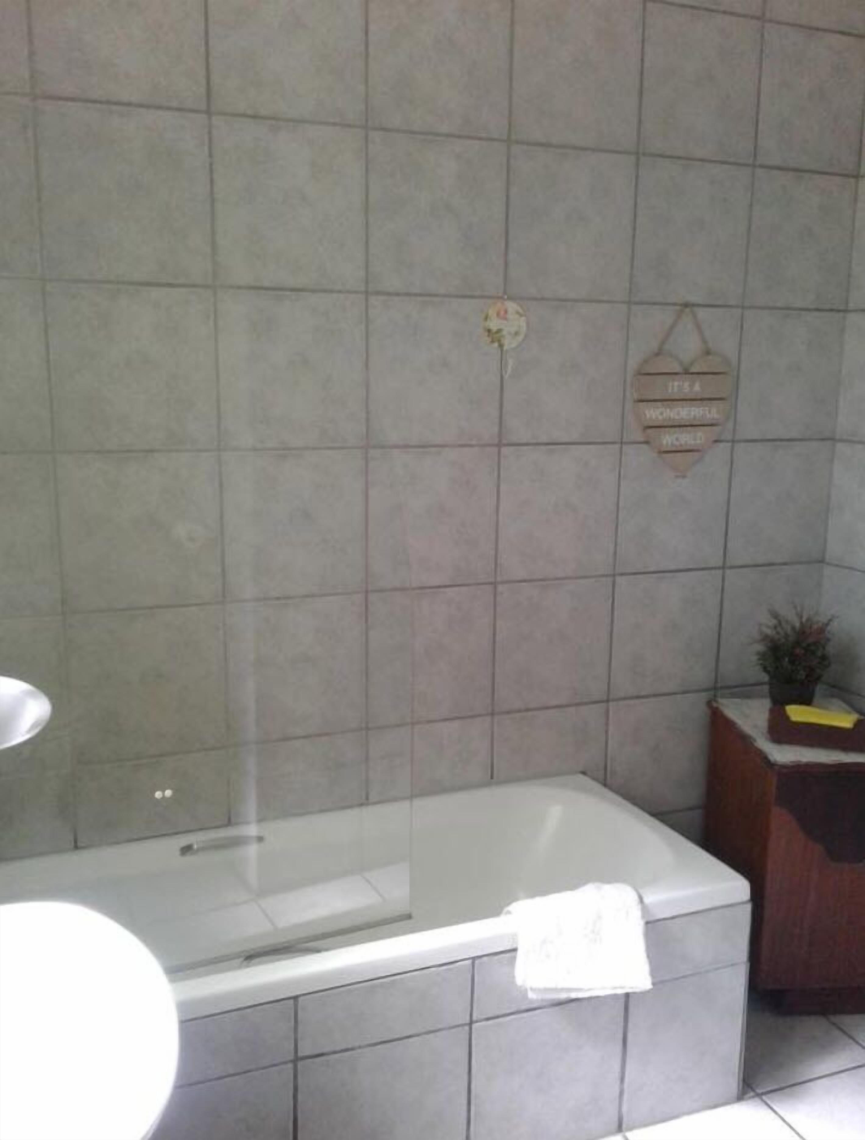 A bathroom with a bathtub, a towel, and a small wooden cabinet with a plant.