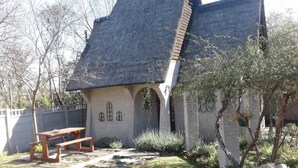 A rustic house with a thatched roof, a stone bench, and a small garden area.