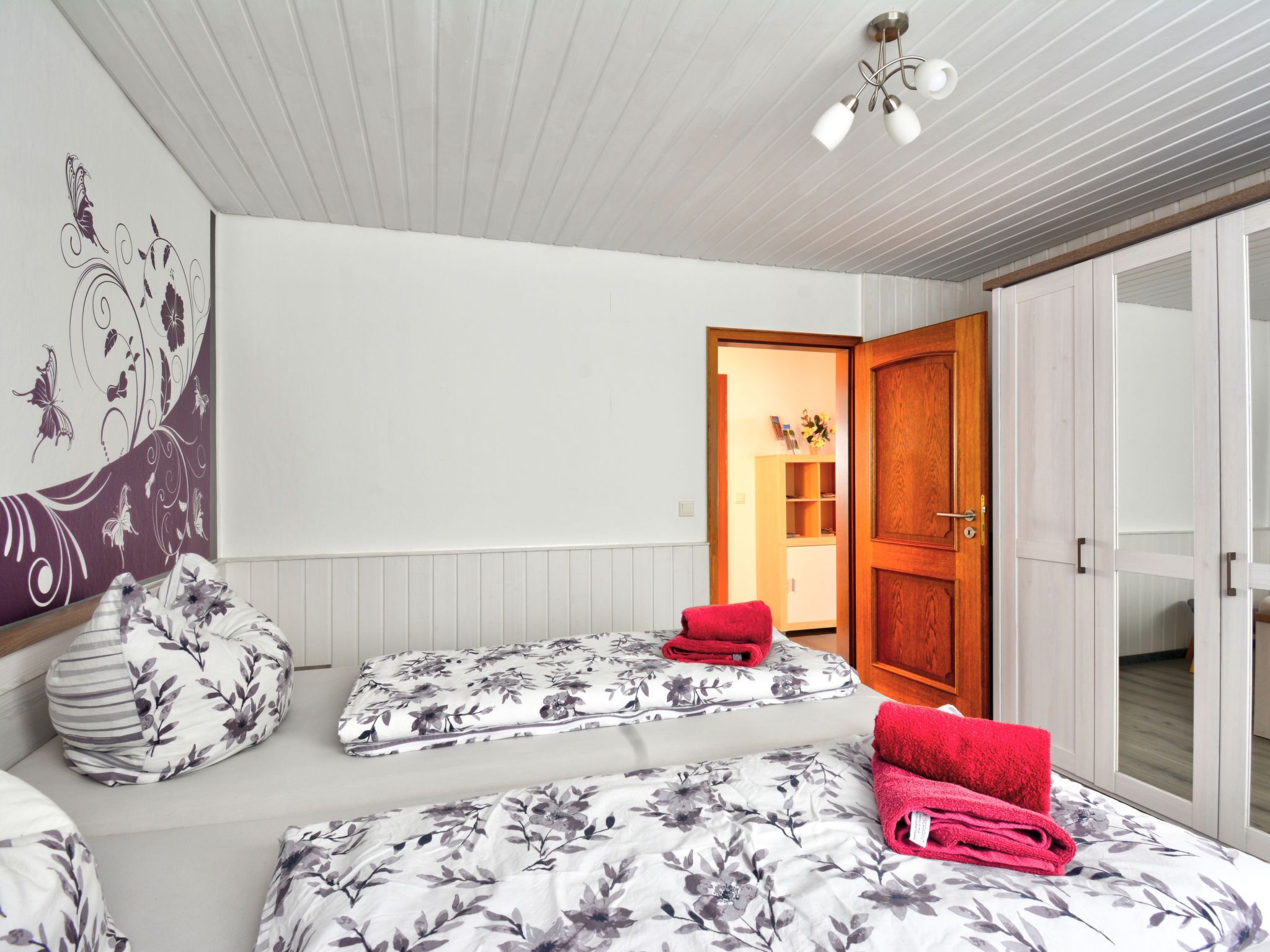 A bedroom with two beds, a wooden door, and a wall with a floral design.