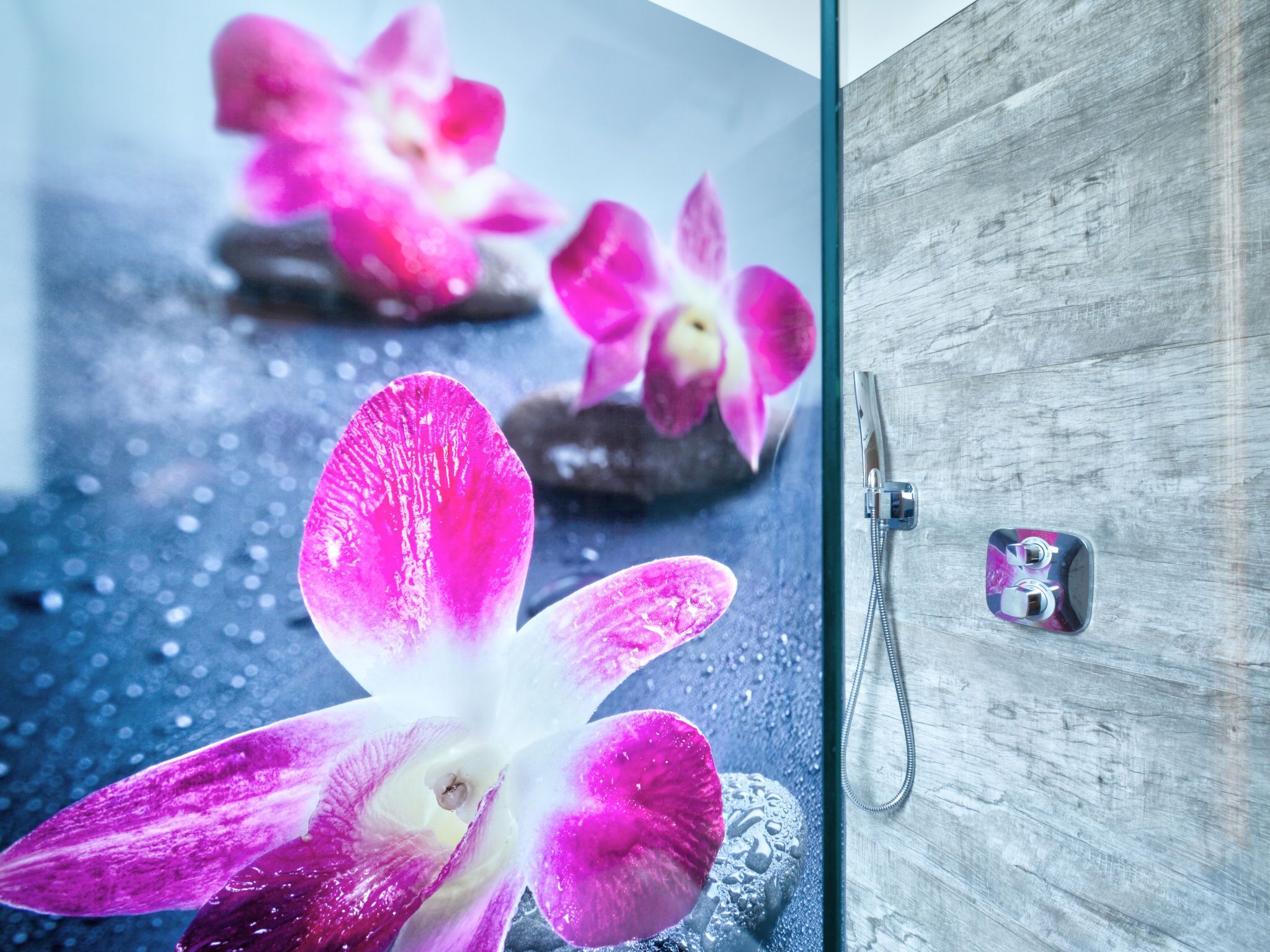 Une salle de bain avec une porte en bois, une douche dotée d’un robinet moderne et des orchidées roses disposées sur le sol.
